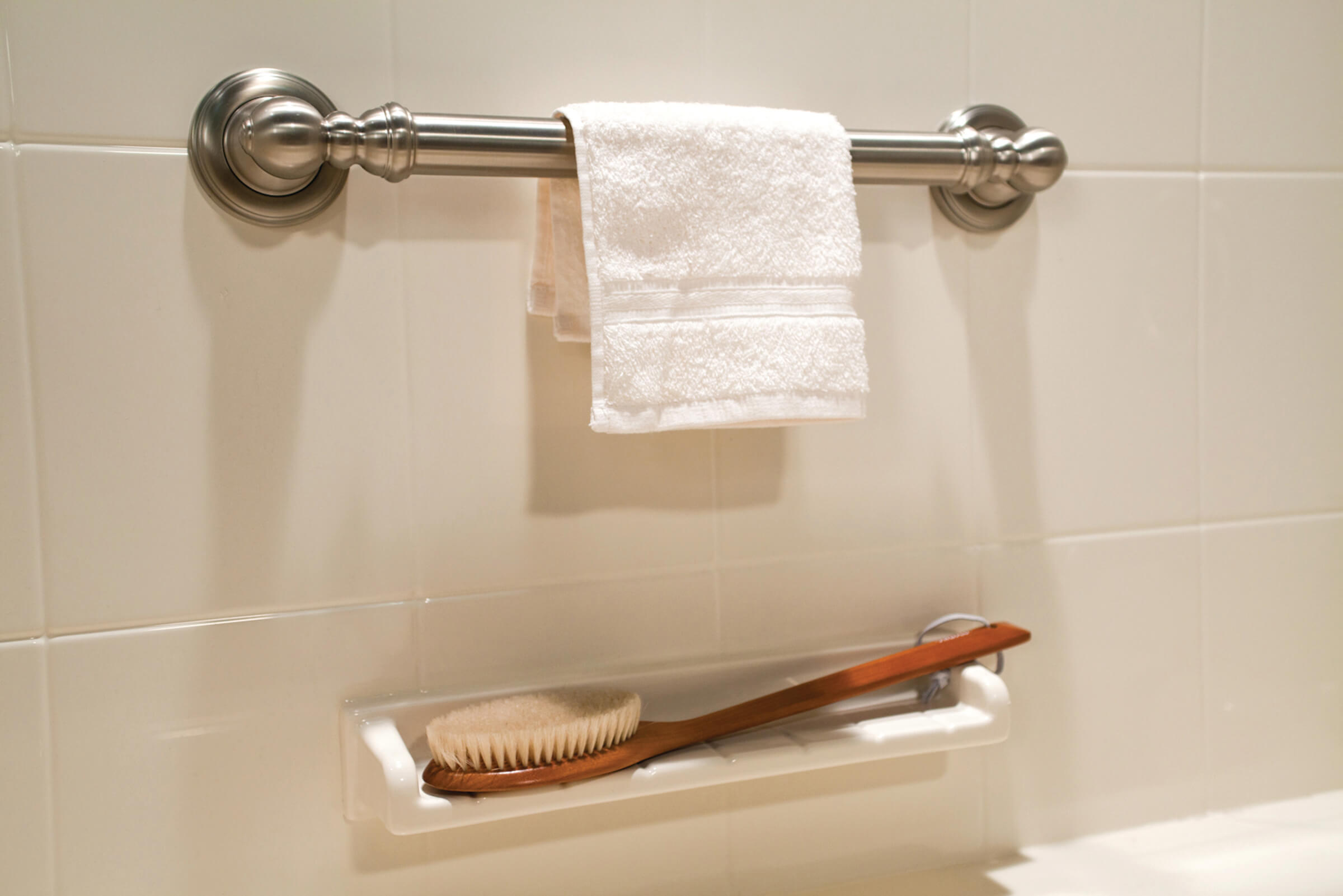 Shower Accessories A white towel neatly hanging on a chrome bathroom towel rack against a light-colored wall.